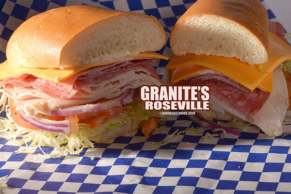 A loaded cold cut Italian sub with lettuce, tomatoes, and provolone on blue checkered paper